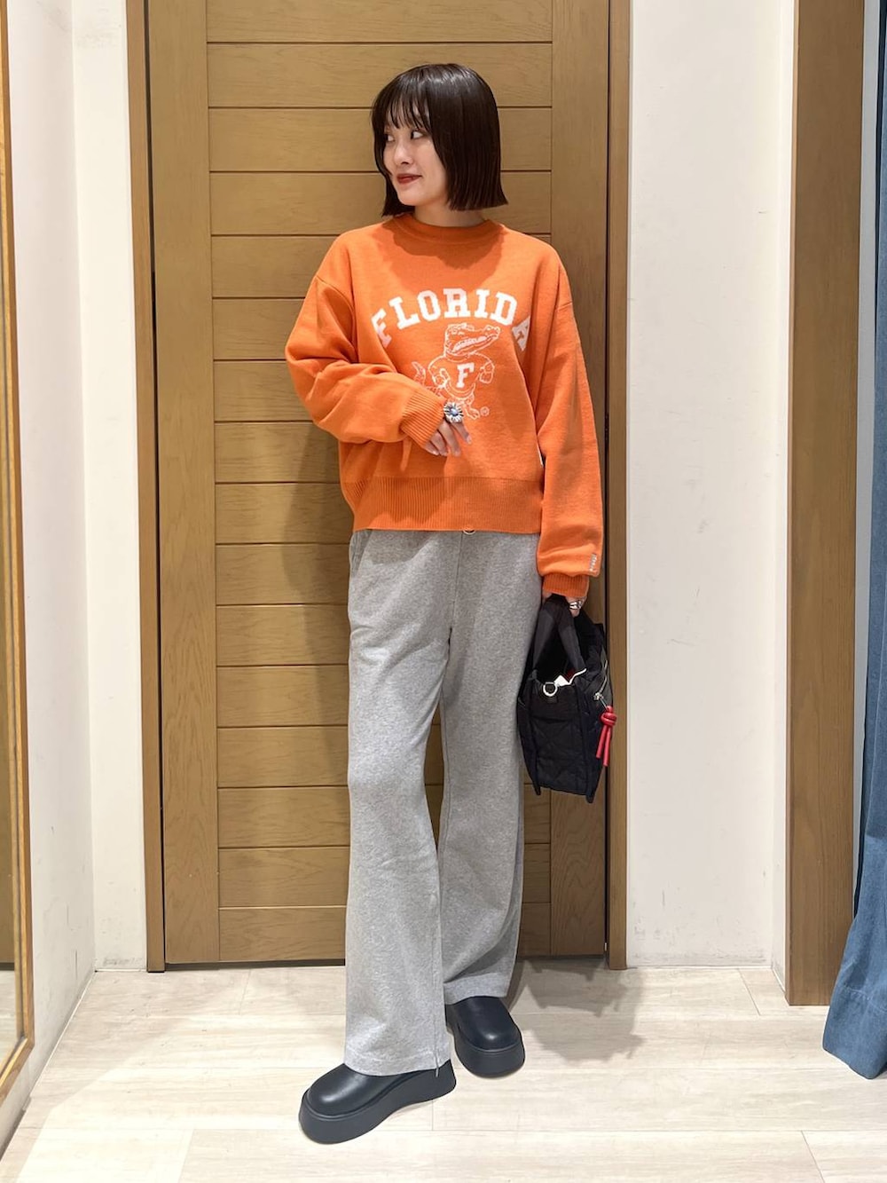 ブラック系のショルダーバッグ、オレンジ系のニット/セーター、グレー系のその他パンツを着用したレディースの秋コーディネートの3枚目の写真