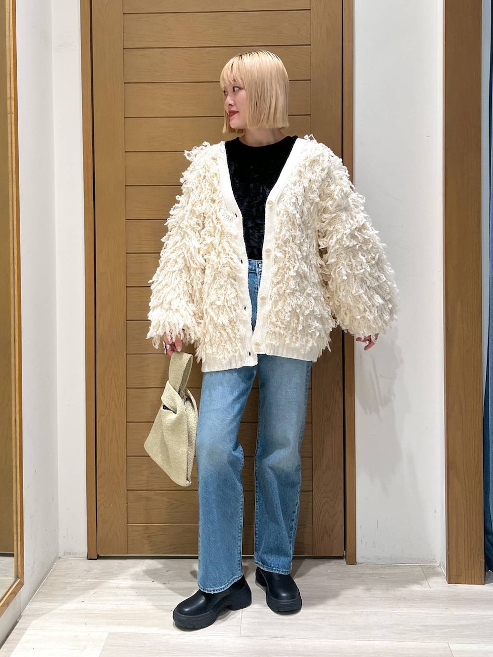 ブルー系のデニムパンツ、ホワイト系のカーディガン/ボレロ、イエロー系のハンドバッグを着用したレディースの冬コーディネートの2枚目の写真