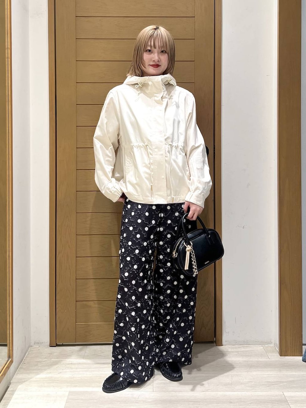 ホワイト系のマウンテンパーカー、ブラック系のローファー、ブラック系のハンドバッグを着用したレディースの春コーディネートの2枚目の写真