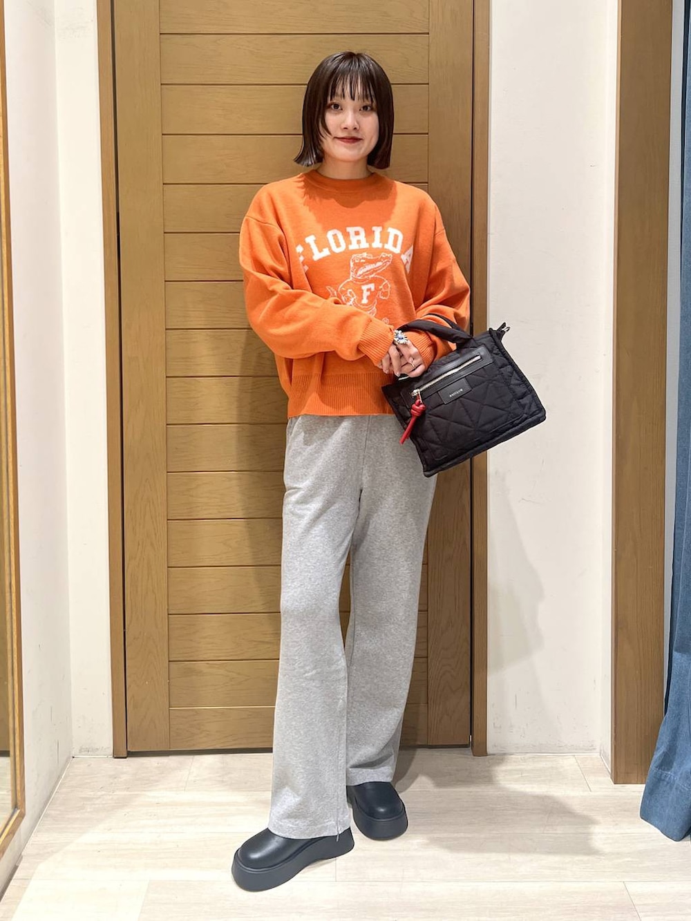 ブラック系のショルダーバッグ、オレンジ系のニット/セーター、グレー系のその他パンツを着用したレディースの秋コーディネートの5枚目の写真