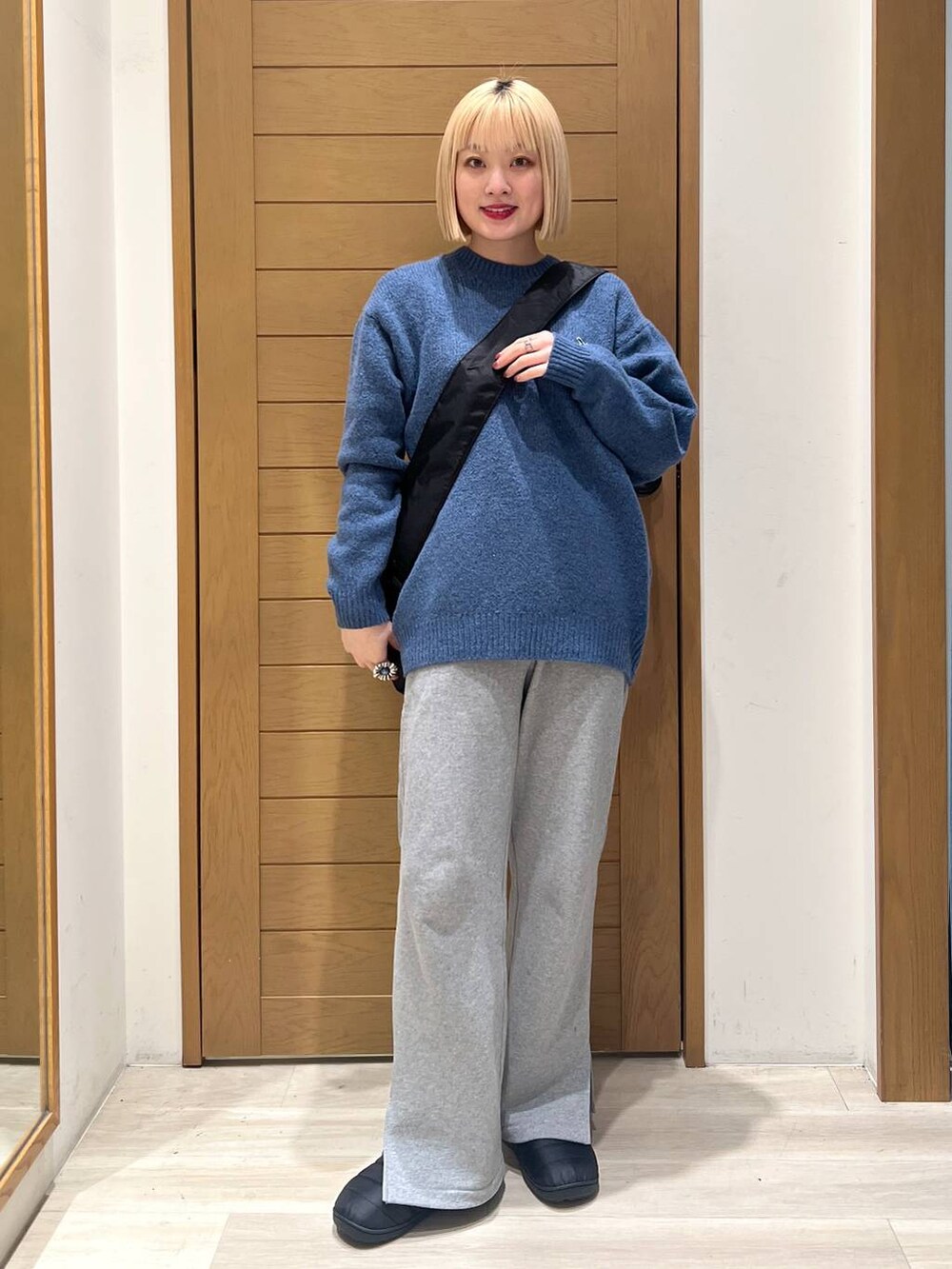 グレー系のスウェットパンツ、ブルー系のニット/セーター、ブラック系のショルダーバッグを着用したレディースの冬コーディネートの2枚目の写真