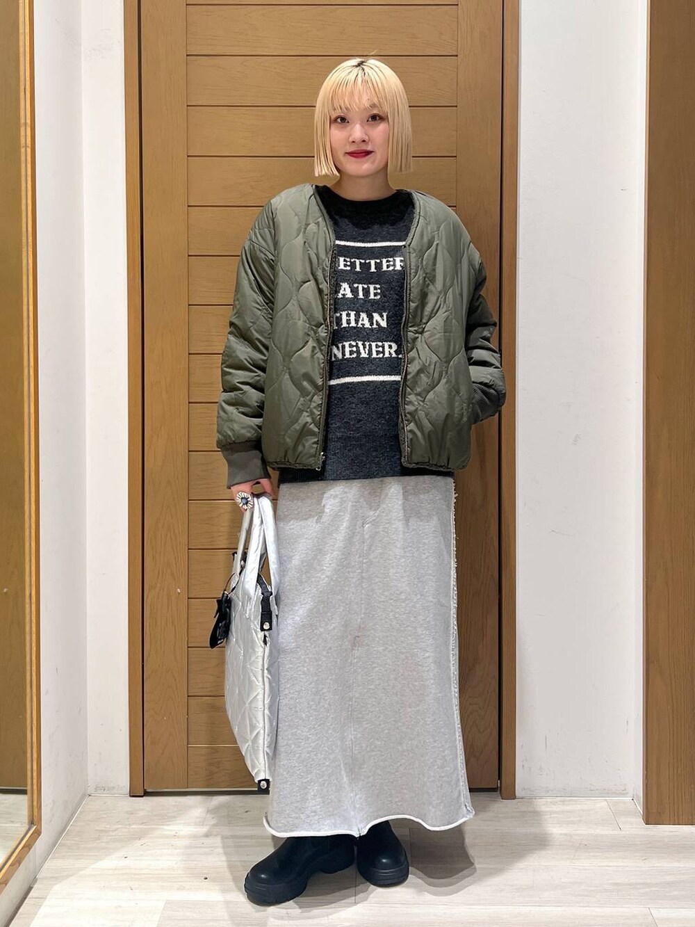 グリーン系のブルゾン、ブラック系のブーツ、シルバー系のトートバッグを着用したレディースの冬コーディネートの2枚目の写真