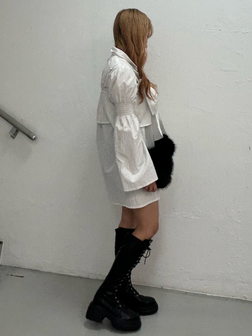 ホワイト系のシャツワンピース、ブラック系のハンドバッグ、ブラック系のブーツを着用したレディースの夏コーディネートの2枚目の写真