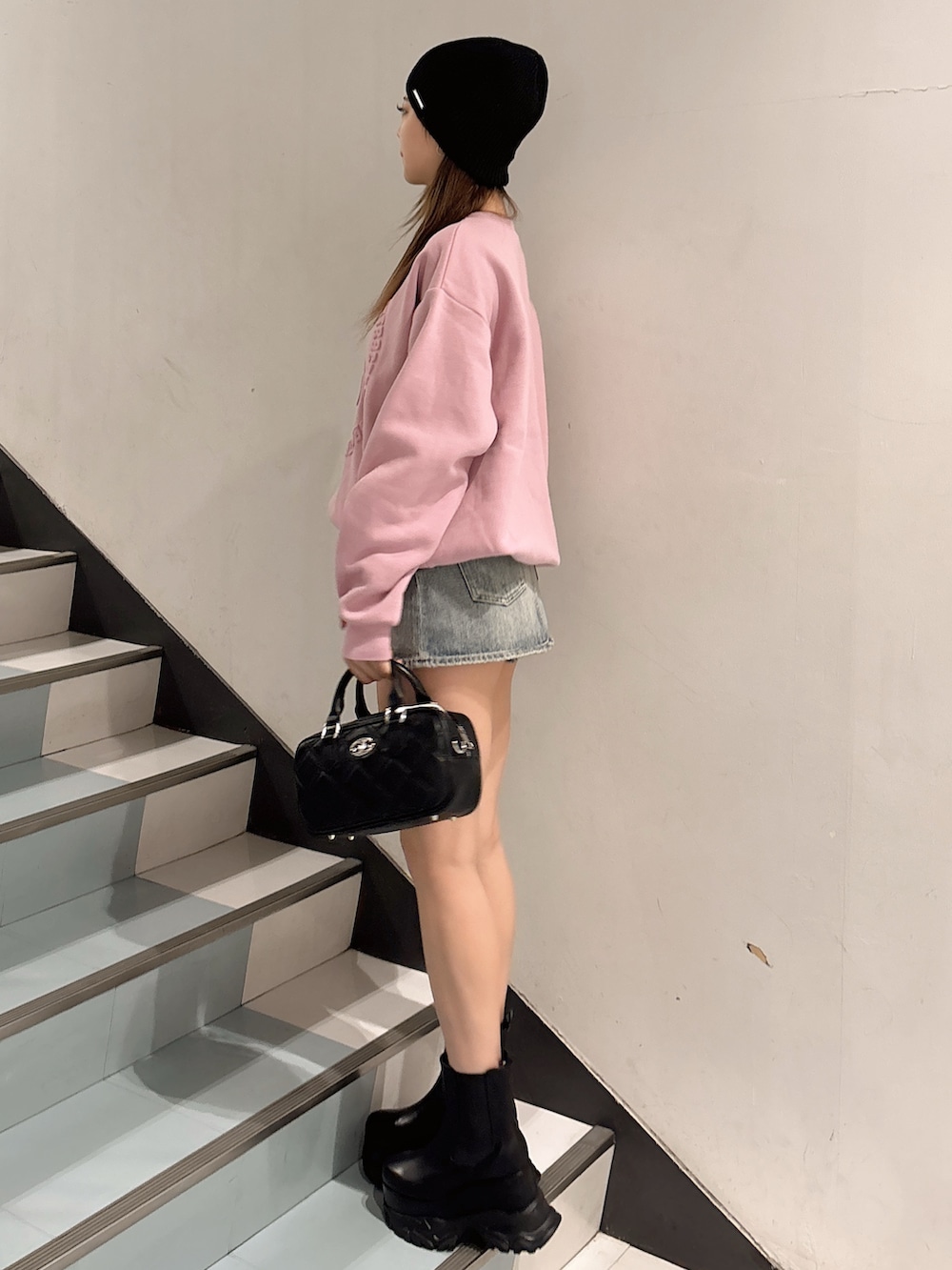 ピンク系のスウェット、ブラック系のハンドバッグ、ブラック系のブーツを着用したレディースの冬コーディネートの2枚目の写真