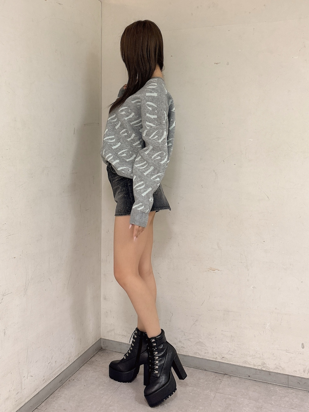 グレー系のニット/セーター、ブラック系のデニムスカート、ブラック系のブーツを着用したレディースの冬コーディネートの2枚目の写真