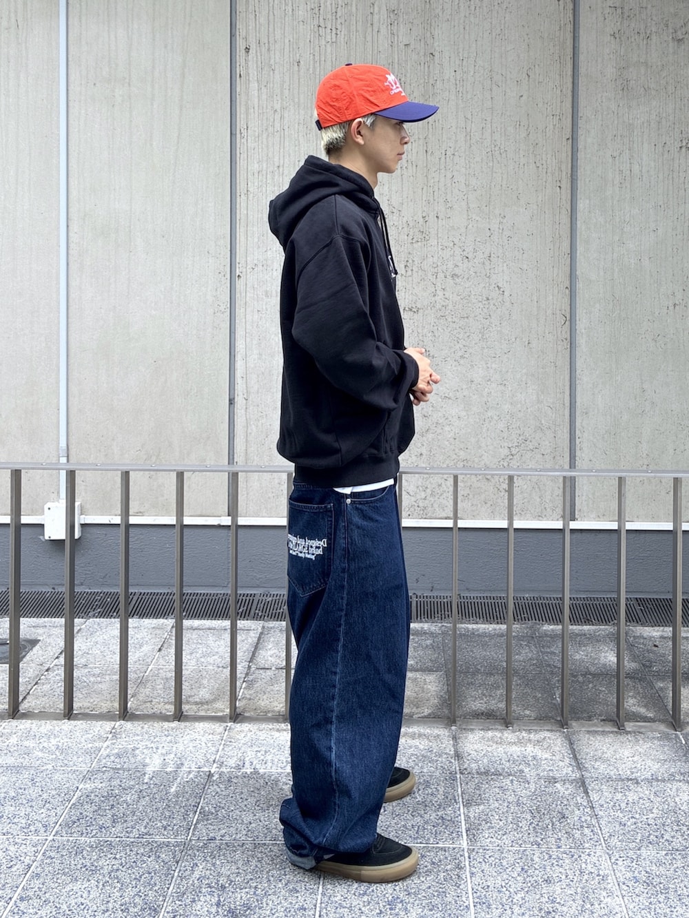 ブラック系のパーカー、ブルー系のデニムパンツ、オレンジ系のキャップを着用したメンズの夏コーディネートの4枚目の写真