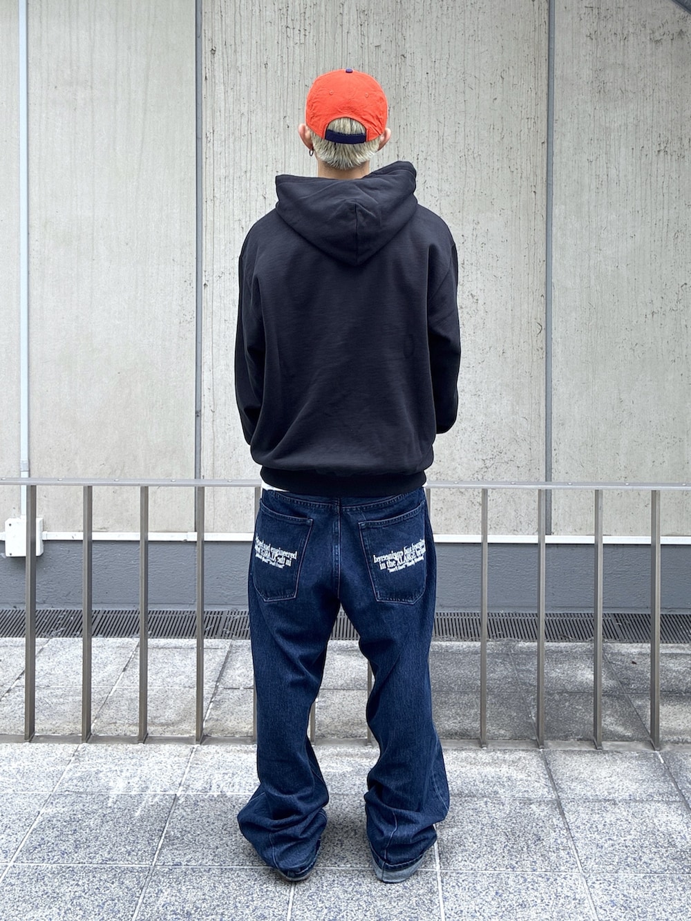 ブラック系のパーカー、ブルー系のデニムパンツ、オレンジ系のキャップを着用したメンズの夏コーディネートの3枚目の写真