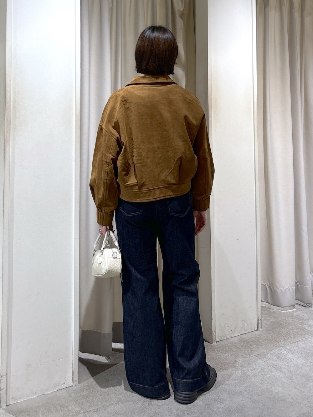 ブラウン系のブルゾン、ホワイト系のニット/セーター、ブルー系のデニムパンツを着用したレディースの秋コーディネートの2枚目の写真