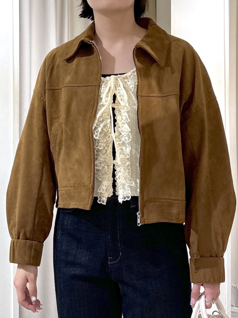 ブラウン系のブルゾン、ホワイト系のニット/セーター、ブルー系のデニムパンツを着用したレディースの秋コーディネートの5枚目の写真