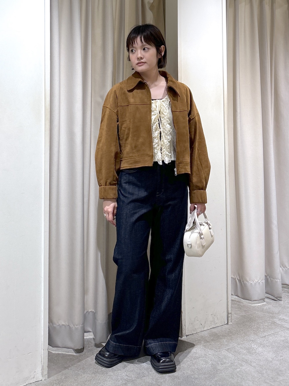 ブラウン系のブルゾン、ホワイト系のニット/セーター、ブルー系のデニムパンツを着用したレディースの秋コーディネートの3枚目の写真