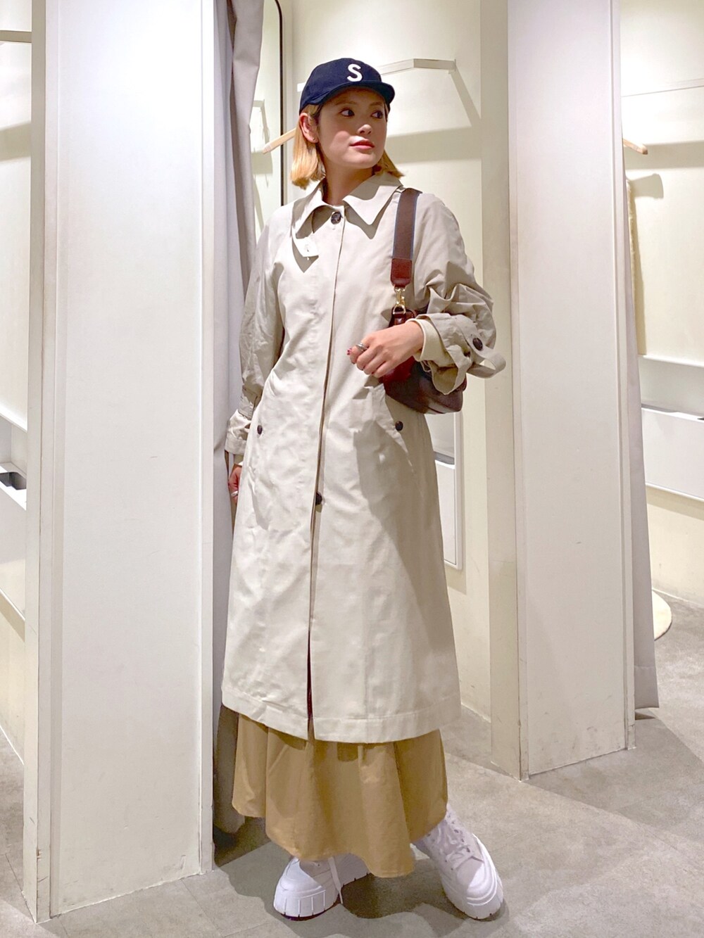 ベージュ系のトレンチコート、ベージュ系のスカート、ブラウン系のショルダーバッグを着用したレディースの冬コーディネートの2枚目の写真