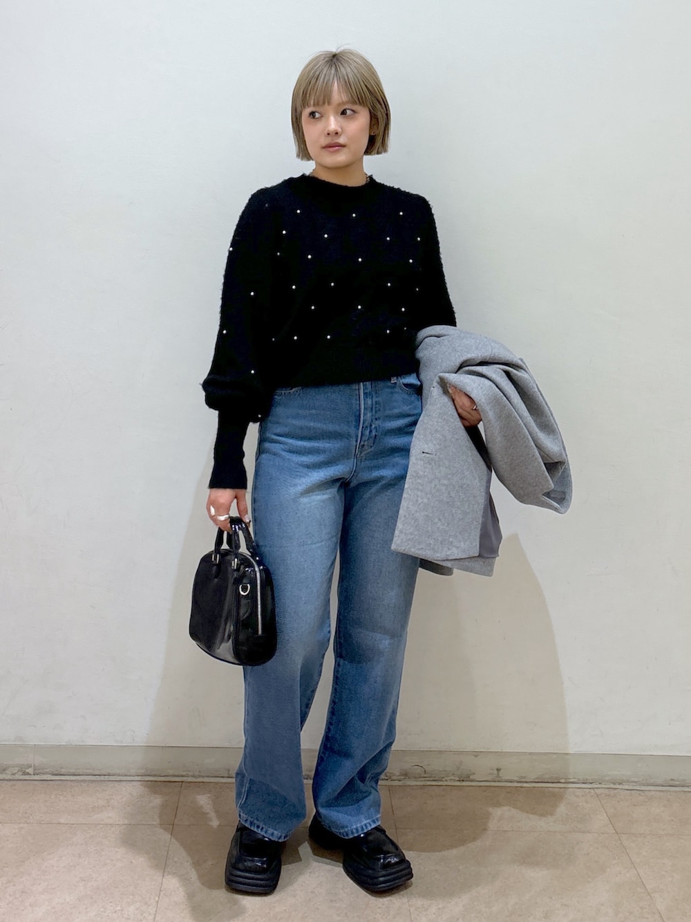 グレー系のピーコート、ブラック系のニット/セーター、ブルー系のデニムパンツを着用したレディースの冬コーディネートの6枚目の写真