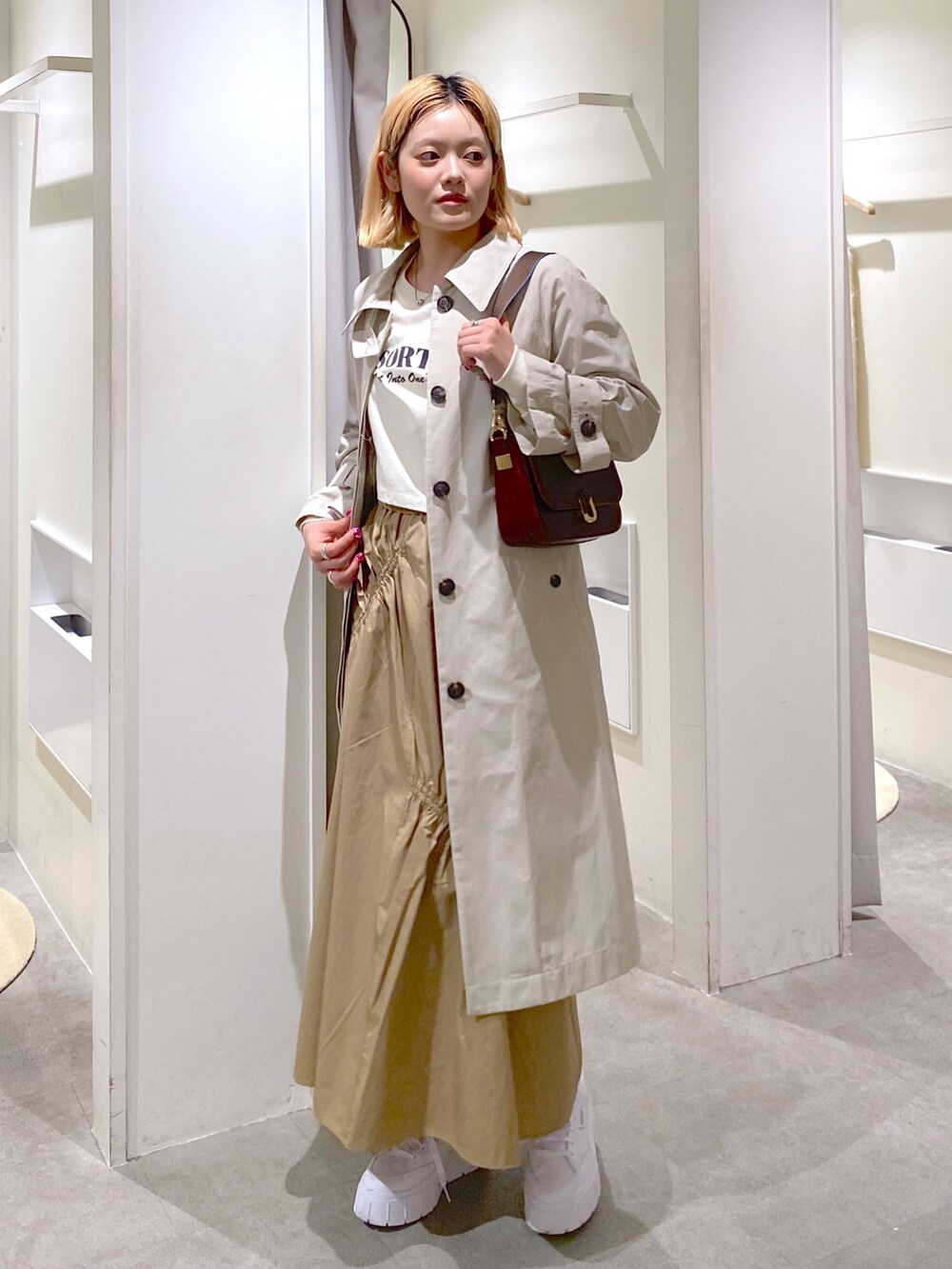 ベージュ系のトレンチコート、ベージュ系のスカート、ブラウン系のショルダーバッグを着用したレディースの冬コーディネートの4枚目の写真