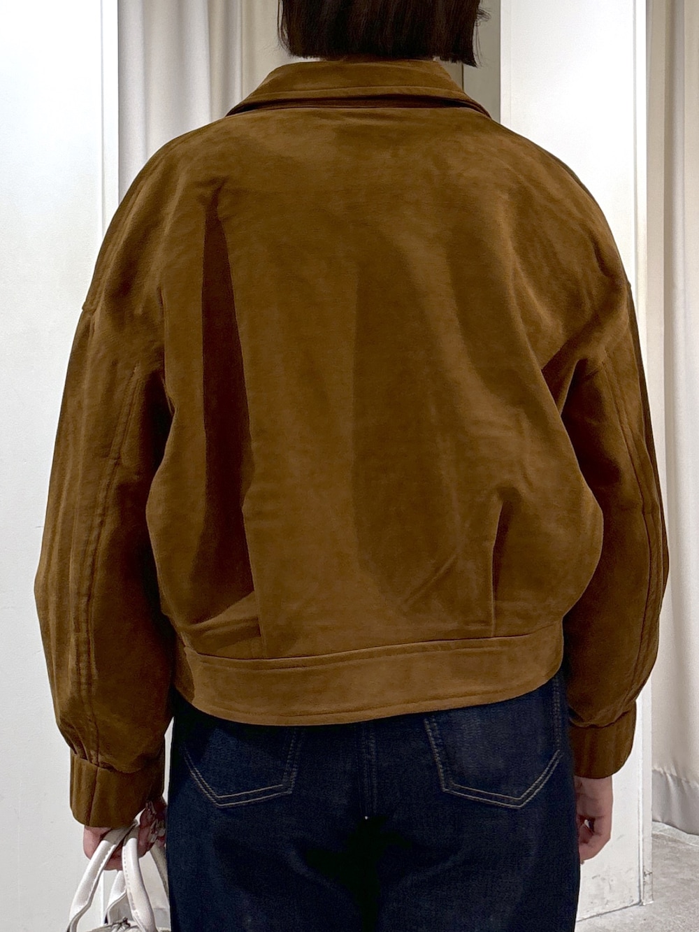 ブラウン系のブルゾン、ホワイト系のニット/セーター、ブルー系のデニムパンツを着用したレディースの秋コーディネートの6枚目の写真