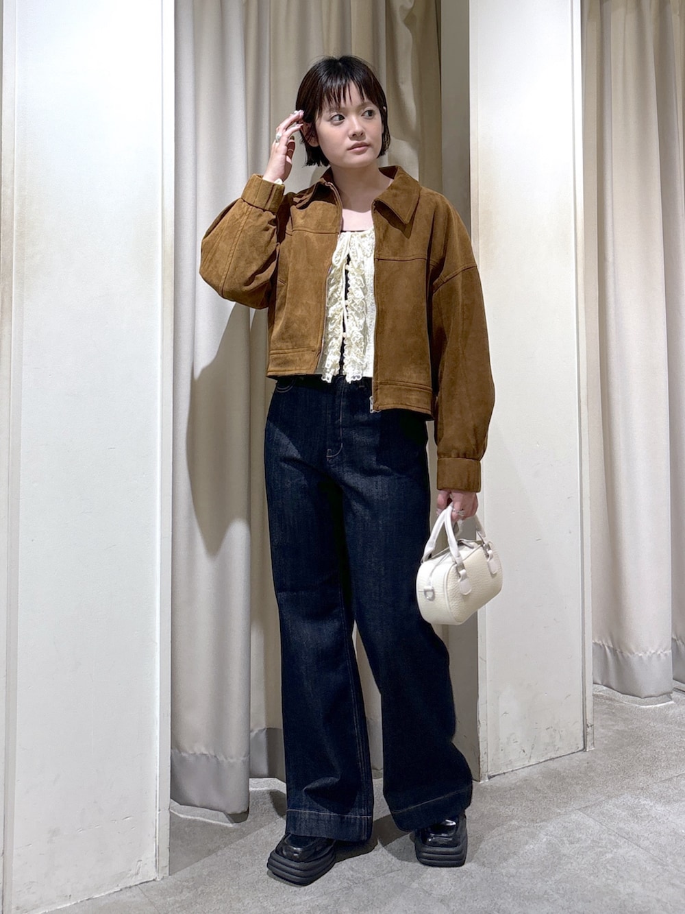 ブラウン系のブルゾン、ホワイト系のニット/セーター、ブルー系のデニムパンツを着用したレディースの秋コーディネートの4枚目の写真