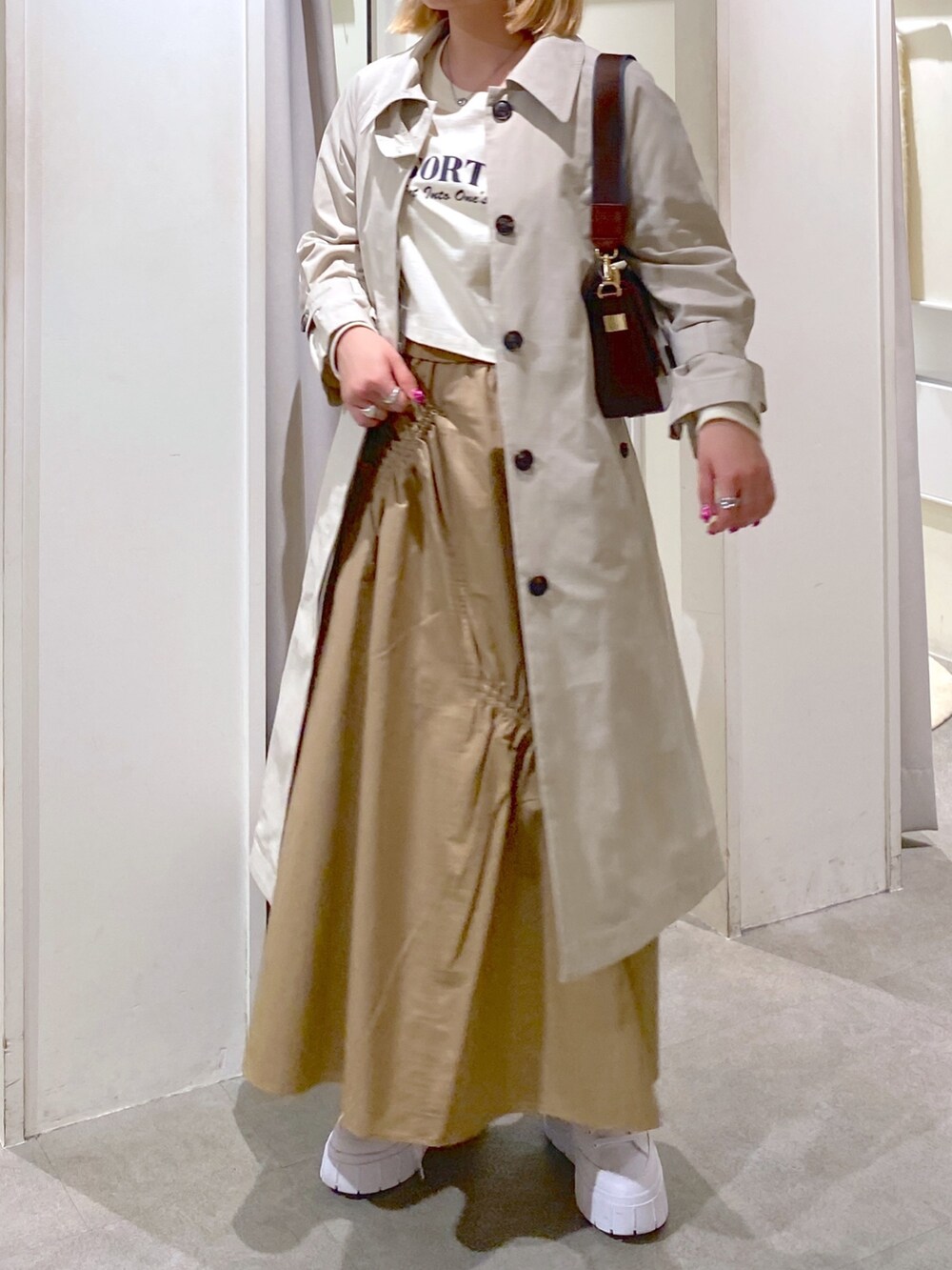 ベージュ系のトレンチコート、ベージュ系のスカート、ブラウン系のショルダーバッグを着用したレディースの冬コーディネートの7枚目の写真