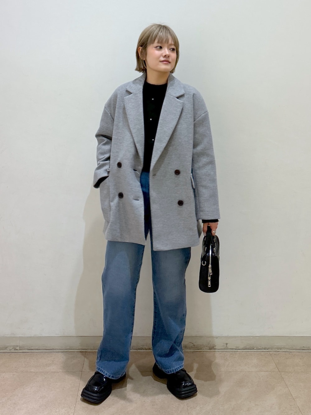 グレー系のピーコート、ブラック系のニット/セーター、ブルー系のデニムパンツを着用したレディースの冬コーディネートの2枚目の写真