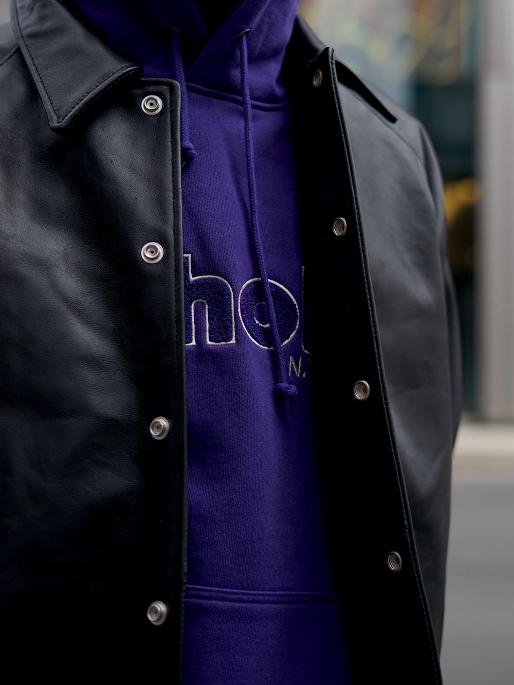 パープル系のパーカー、ブラック系のライダースジャケット、ブルー系のスウェットパンツを着用したメンズの秋コーディネートの2枚目の写真