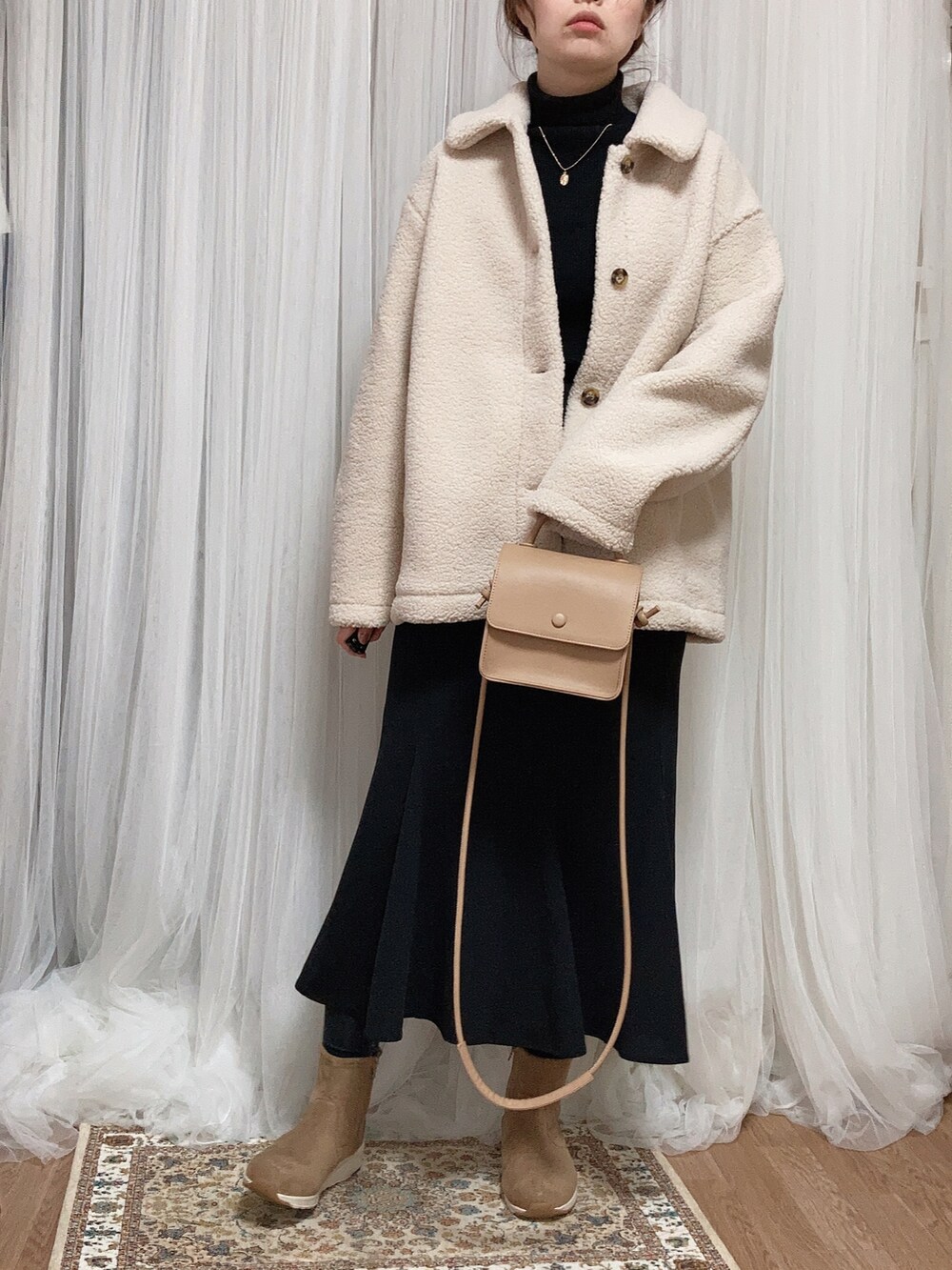 ホワイト系のステンカラーコート、ベージュ系のショルダーバッグ、ブラック系のスカートを着用したレディースの冬コーディネートの2枚目の写真