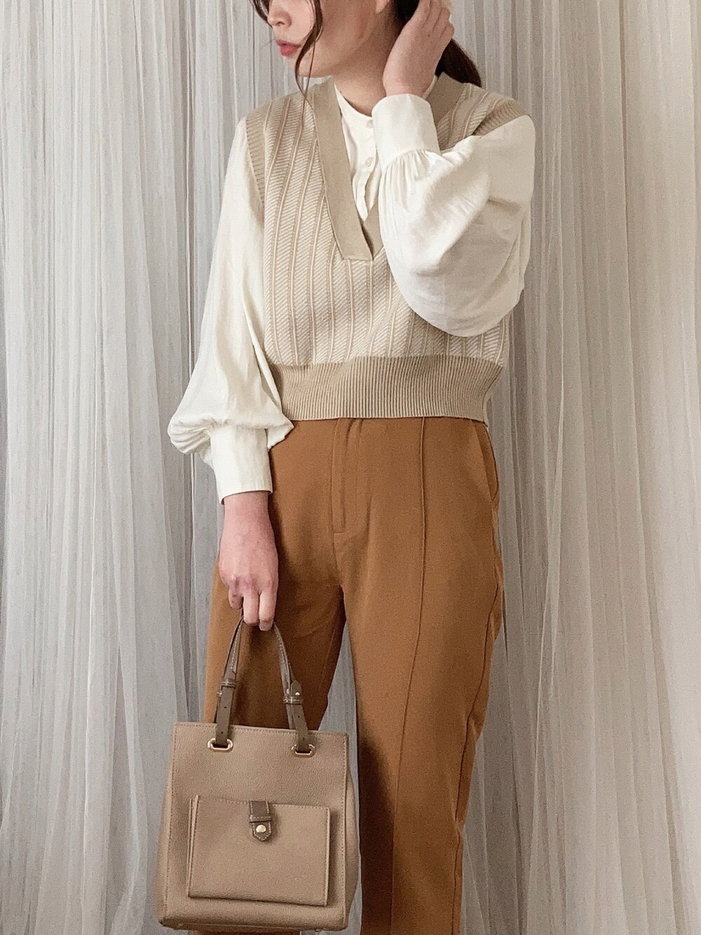 ベージュ系のバッグ、ホワイト系のパンプス、ベージュ系のベストを着用したレディースの春コーディネートの2枚目の写真