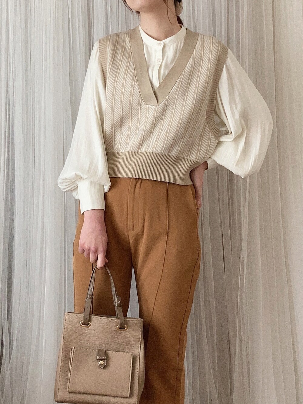 ベージュ系のバッグ、ホワイト系のパンプス、ベージュ系のベストを着用したレディースの春コーディネートの4枚目の写真