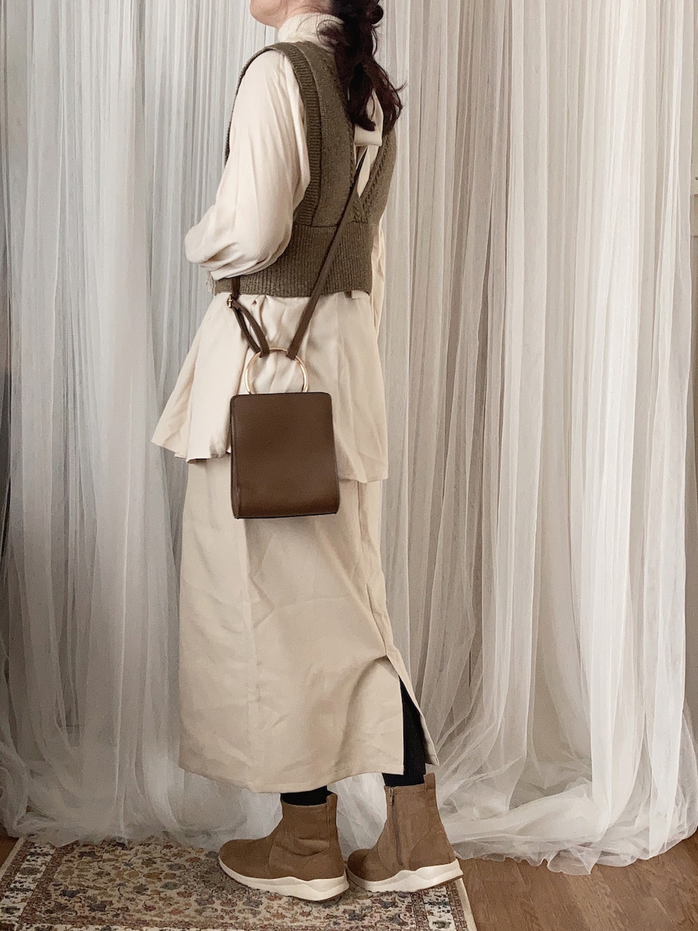 ブラウン系のステンカラーコート、ブラウン系のベスト、ブラウン系のショルダーバッグを着用したレディースの冬コーディネートの3枚目の写真