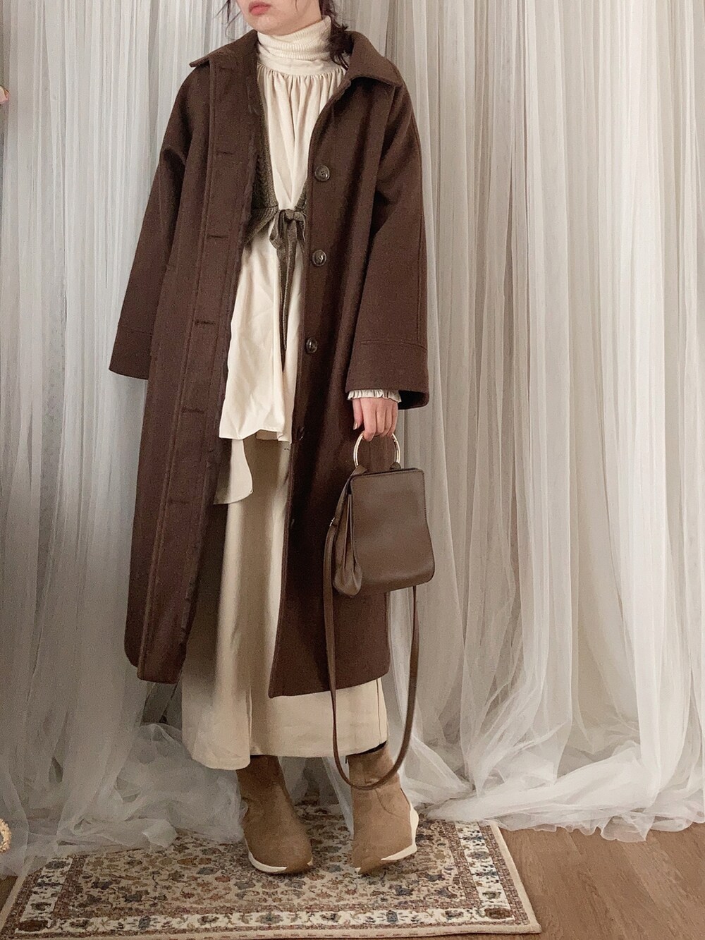 ブラウン系のステンカラーコート、ブラウン系のベスト、ブラウン系のショルダーバッグを着用したレディースの冬コーディネートの2枚目の写真