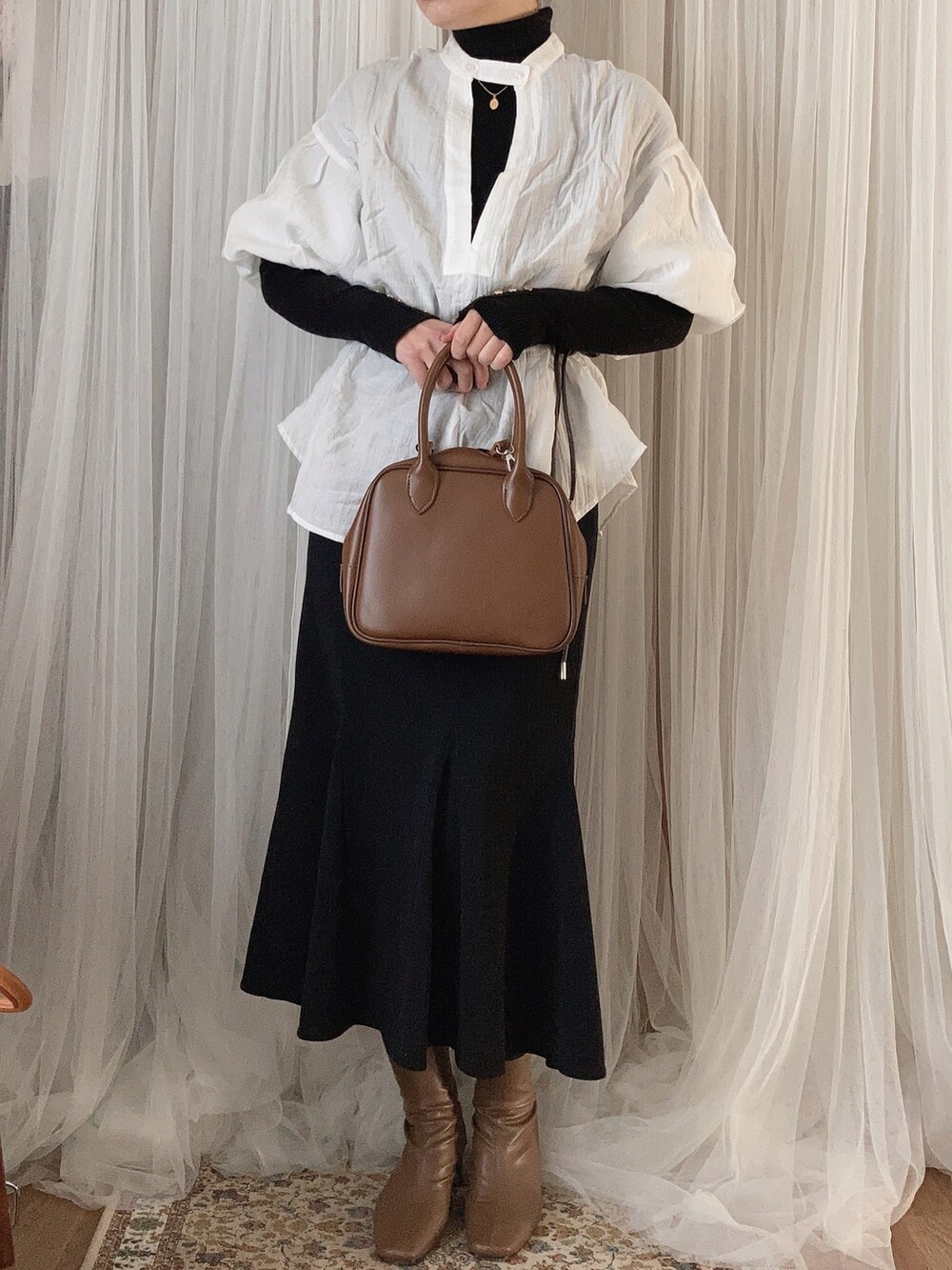 ブラウン系のボストンバッグ、ブラック系のスカート、ブラウン系のブーツを着用したレディースの冬コーディネートの2枚目の写真