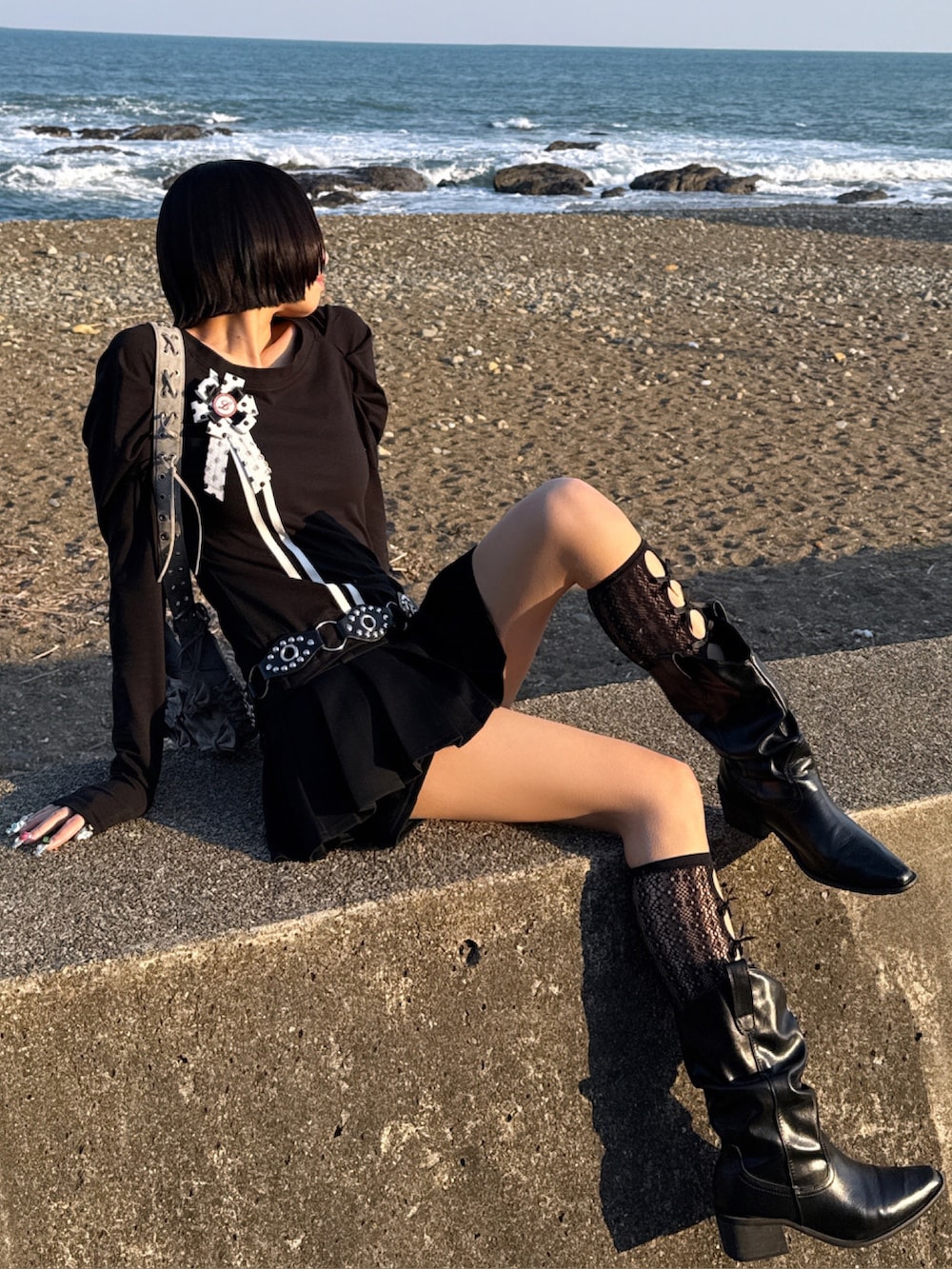 ブラック系のトップス、ブラック系のハンドバッグ、ブラック系のブーツを着用したレディースの春コーディネートの2枚目の写真