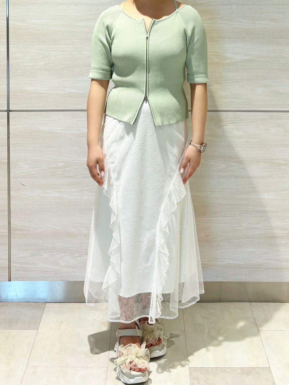 グリーン系のニット/セーター、ホワイト系のスカートを着用したレディースの春コーディネートの2枚目の写真