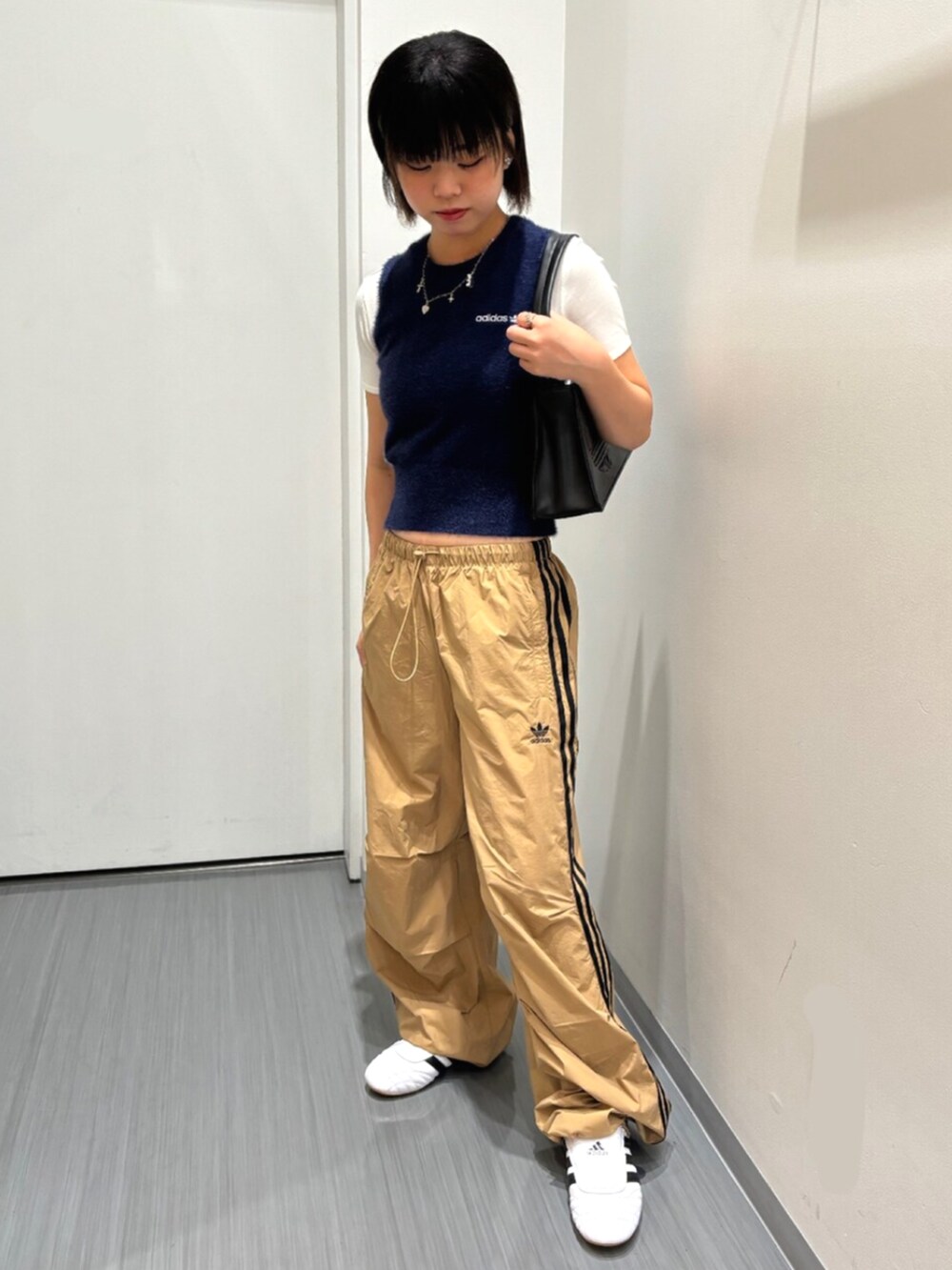 ブルー系のベスト、ブラック系のショルダーバッグ、ホワイト系のシューズを着用したレディースの秋コーディネートの2枚目の写真