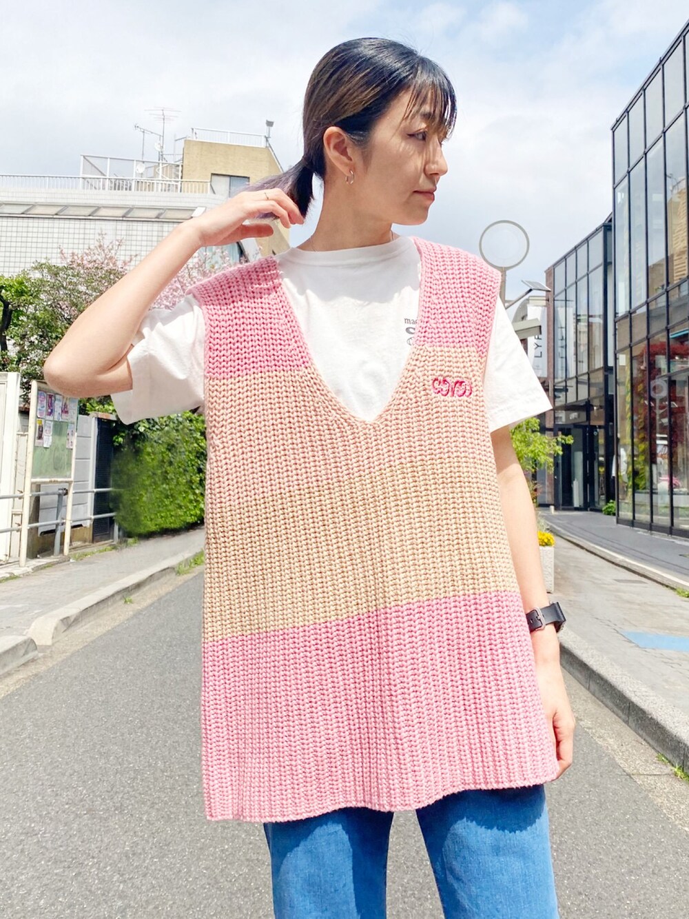 ブラック系のスニーカー、ブルー系のデニムパンツ、ピンク系のベストを着用したレディースの春コーディネートの3枚目の写真
