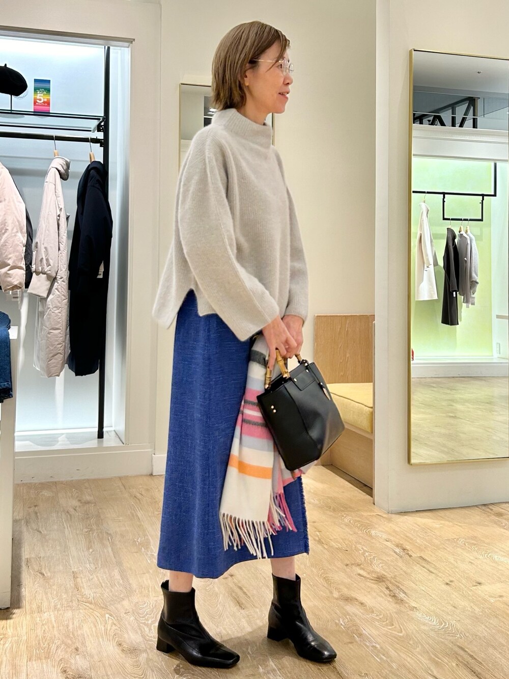 ブルー系のスカート、ブラック系のショルダーバッグ、ベージュ系のニット/セーターを着用したレディースの冬コーディネートの2枚目の写真