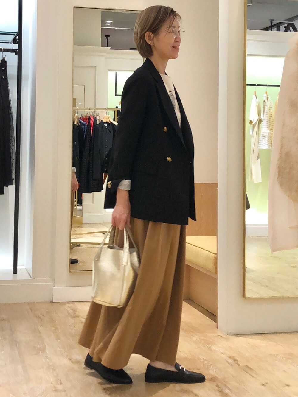 イエロー系のスカート、ゴールド系のトートバッグ、ブラック系のテーラードジャケットを着用したレディースの秋コーディネートの3枚目の写真