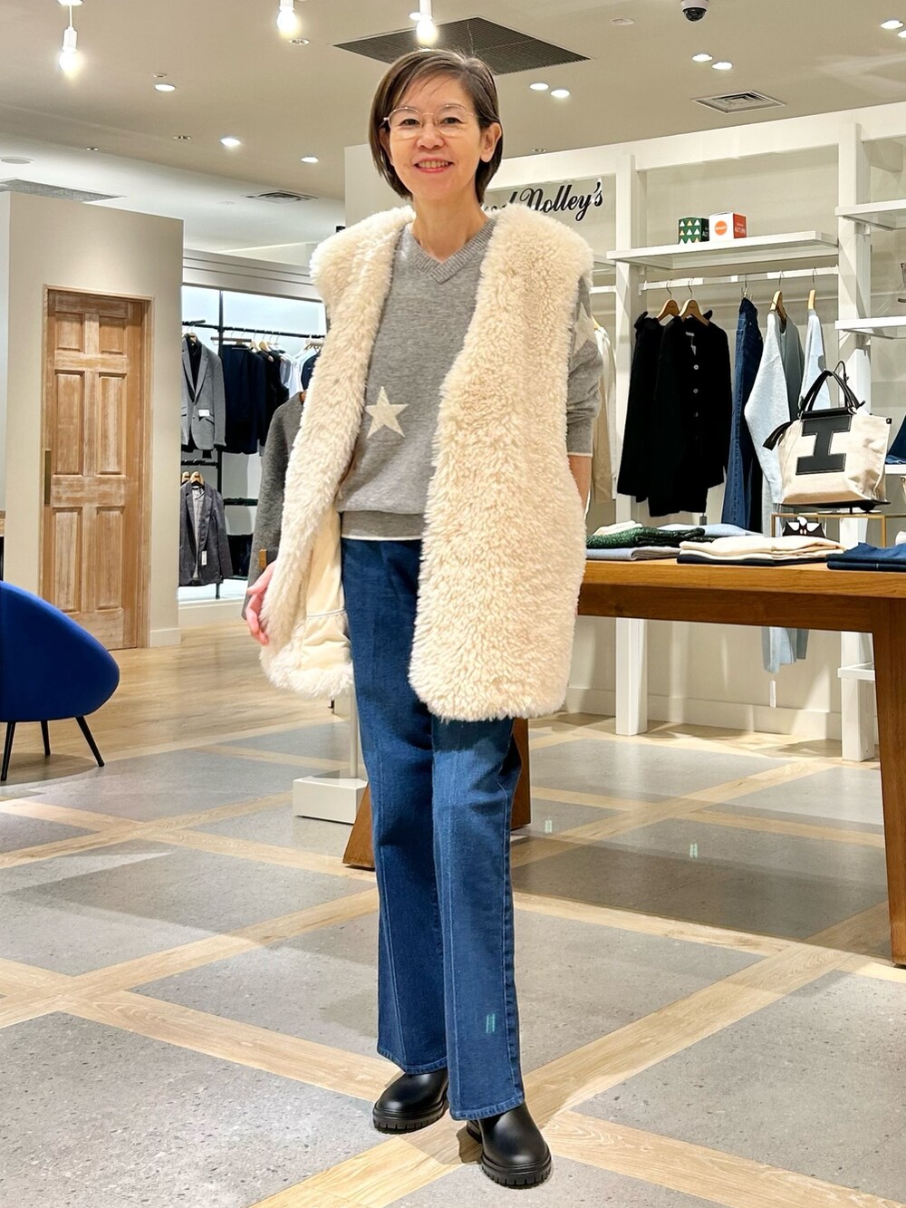 ホワイト系のベスト、グレー系のニット/セーター、ブルー系のデニムパンツを着用したレディースの秋コーディネートの2枚目の写真