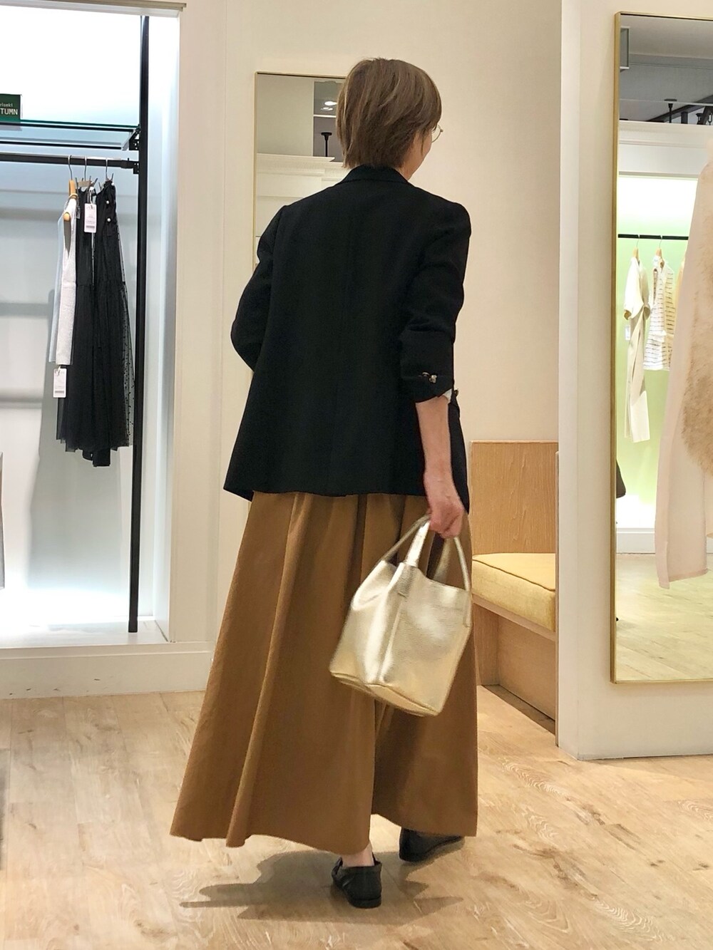 イエロー系のスカート、ゴールド系のトートバッグ、ブラック系のテーラードジャケットを着用したレディースの秋コーディネートの4枚目の写真
