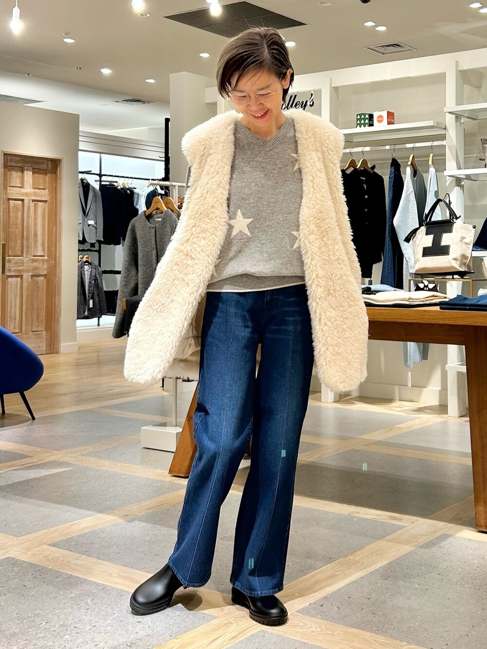 ホワイト系のベスト、グレー系のニット/セーター、ブルー系のデニムパンツを着用したレディースの秋コーディネートの4枚目の写真