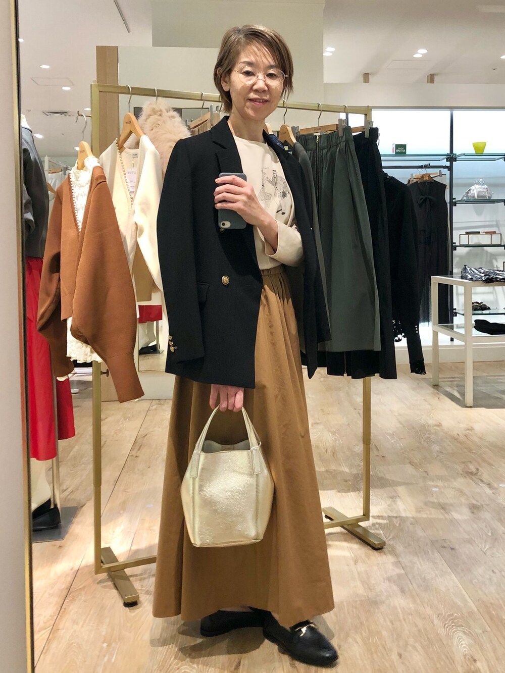 イエロー系のスカート、ゴールド系のトートバッグ、ブラック系のテーラードジャケットを着用したレディースの秋コーディネートの6枚目の写真