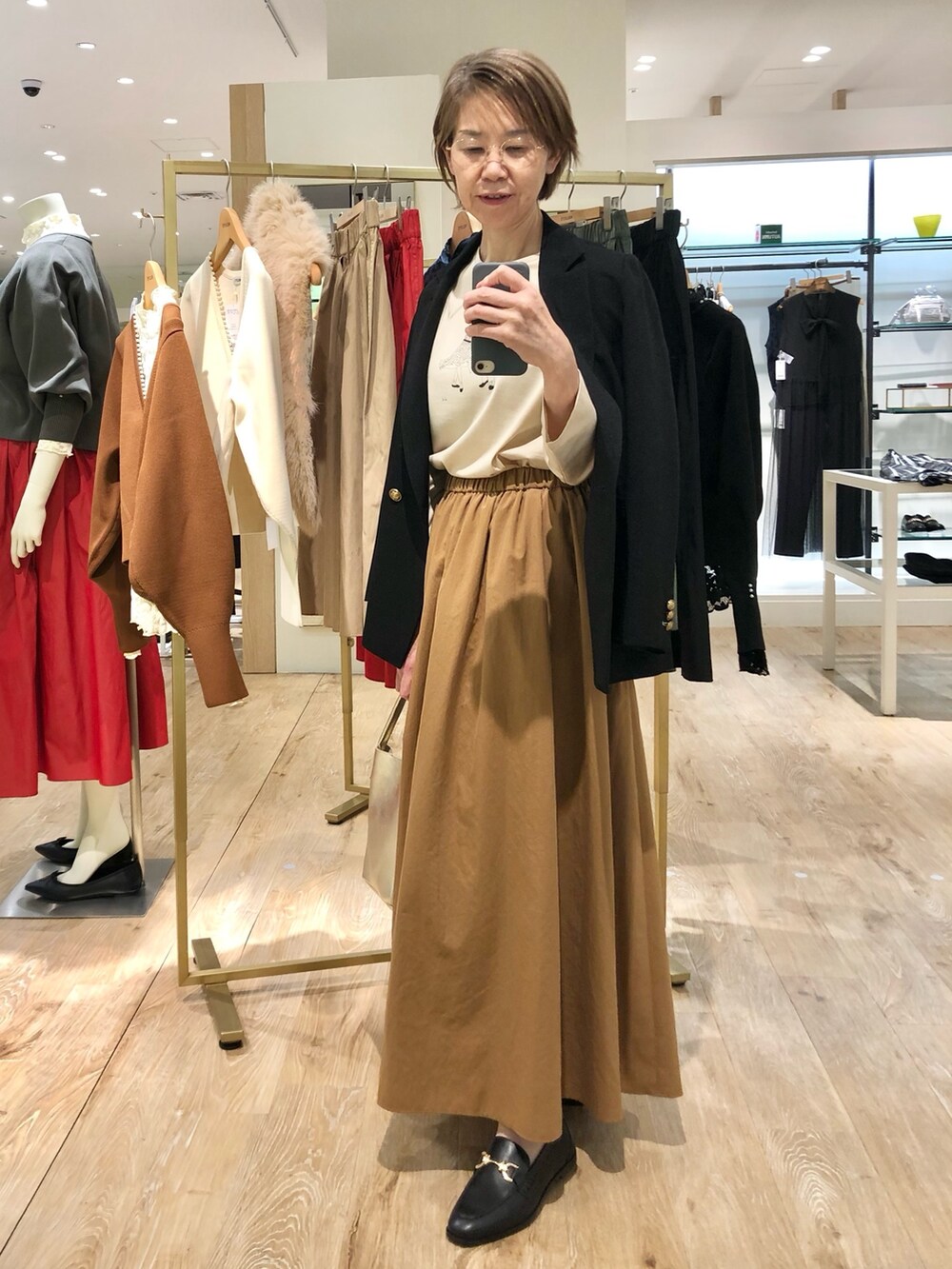 イエロー系のスカート、ゴールド系のトートバッグ、ブラック系のテーラードジャケットを着用したレディースの秋コーディネートの7枚目の写真