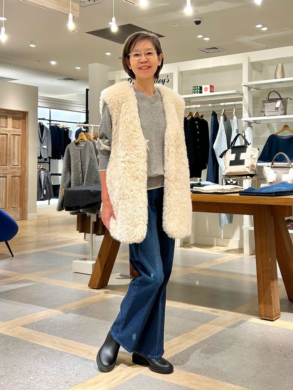 ホワイト系のベスト、グレー系のニット/セーター、ブルー系のデニムパンツを着用したレディースの秋コーディネートの3枚目の写真