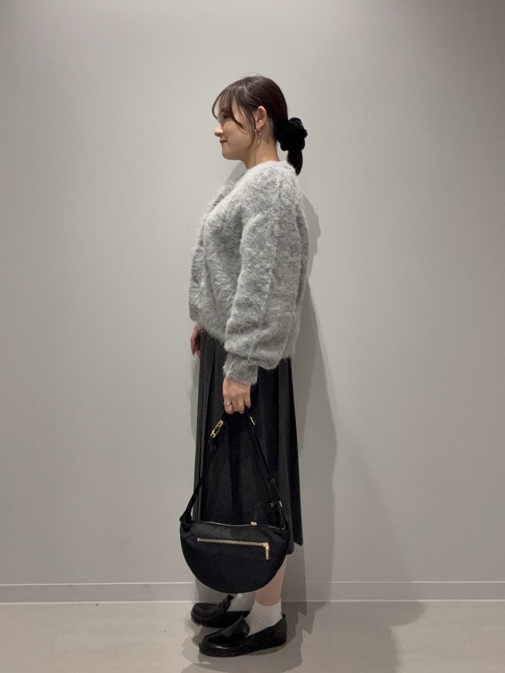 グレー系のスカート、グレー系のカーディガン/ボレロ、ブラック系のショルダーバッグを着用したレディースの秋コーディネートの2枚目の写真