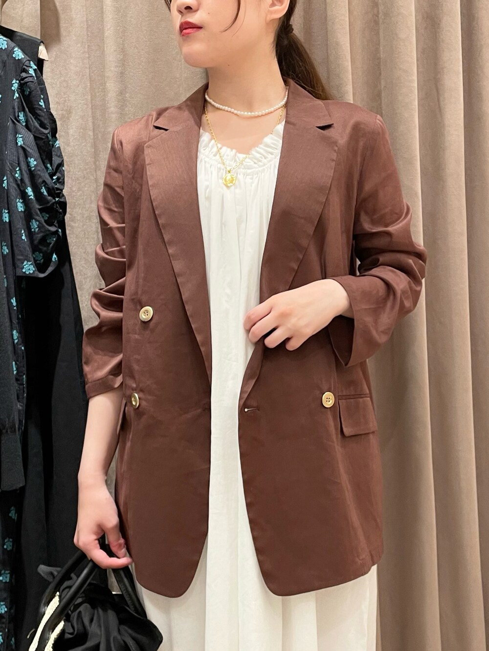 ブラウン系のテーラードジャケット、ホワイト系のワンピース、ブラック系のショルダーバッグを着用したレディースの夏コーディネートの3枚目の写真