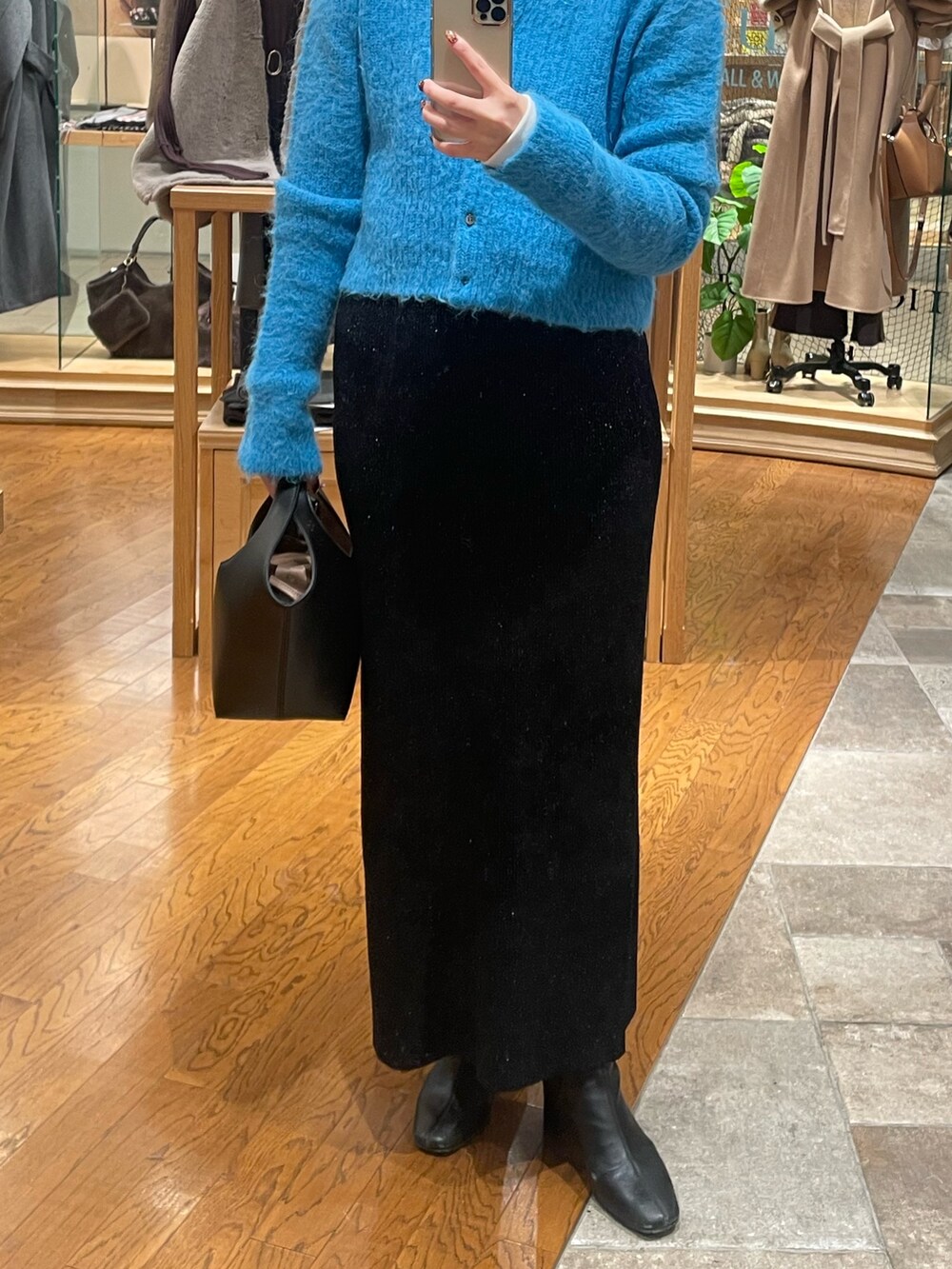 ブラック系のスカート、ブラック系のハンドバッグ、ブルー系のカーディガン/ボレロを着用したレディースの秋コーディネートの3枚目の写真