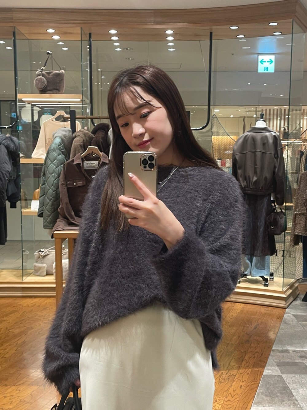 グレー系のニット/セーター、ホワイト系のスカート、ブラック系のブーツを着用したレディースの秋コーディネートの2枚目の写真