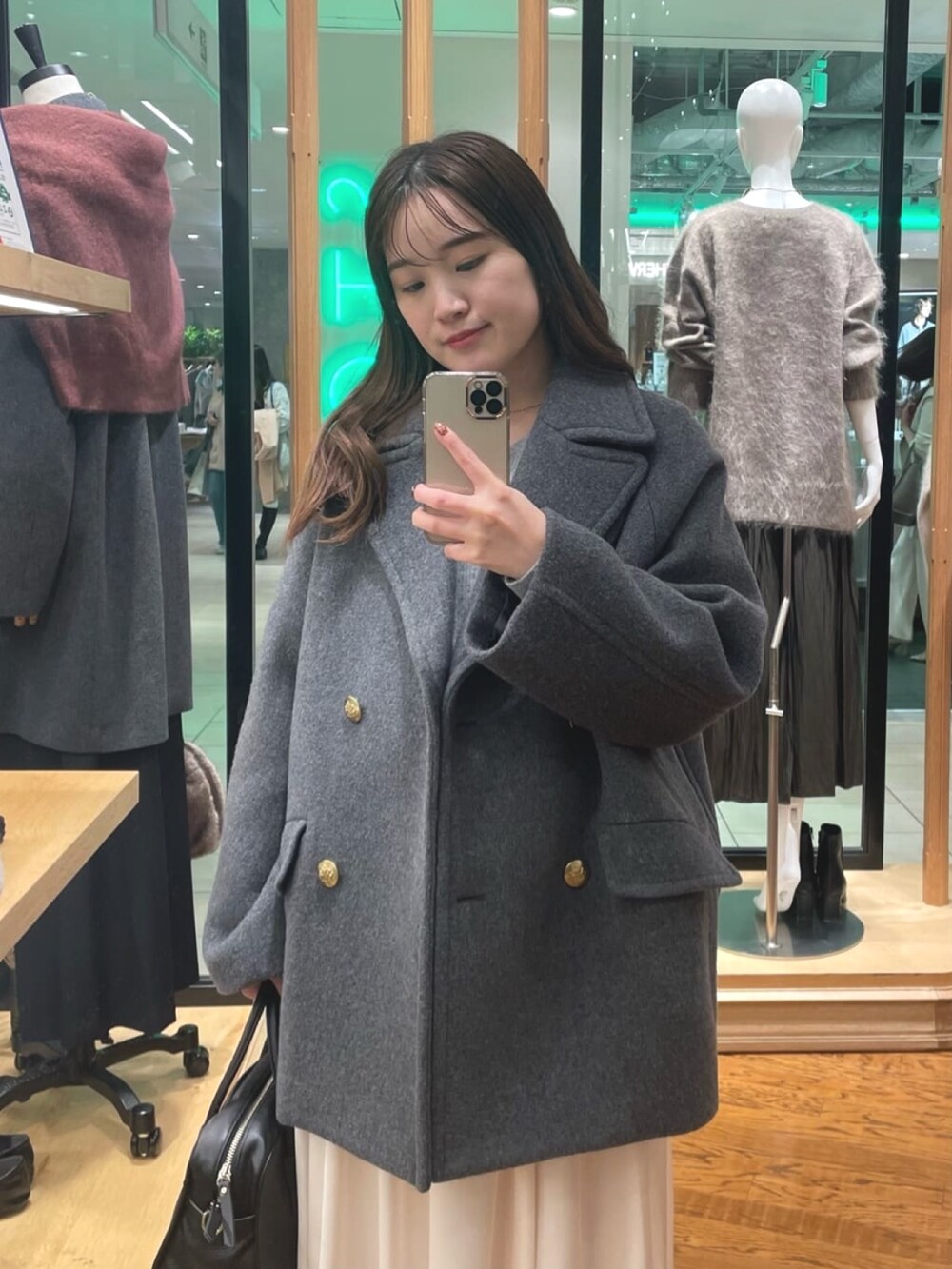 グレー系のピーコート、ホワイト系のスカート、ブラック系のボストンバッグを着用したレディースの秋コーディネートの2枚目の写真