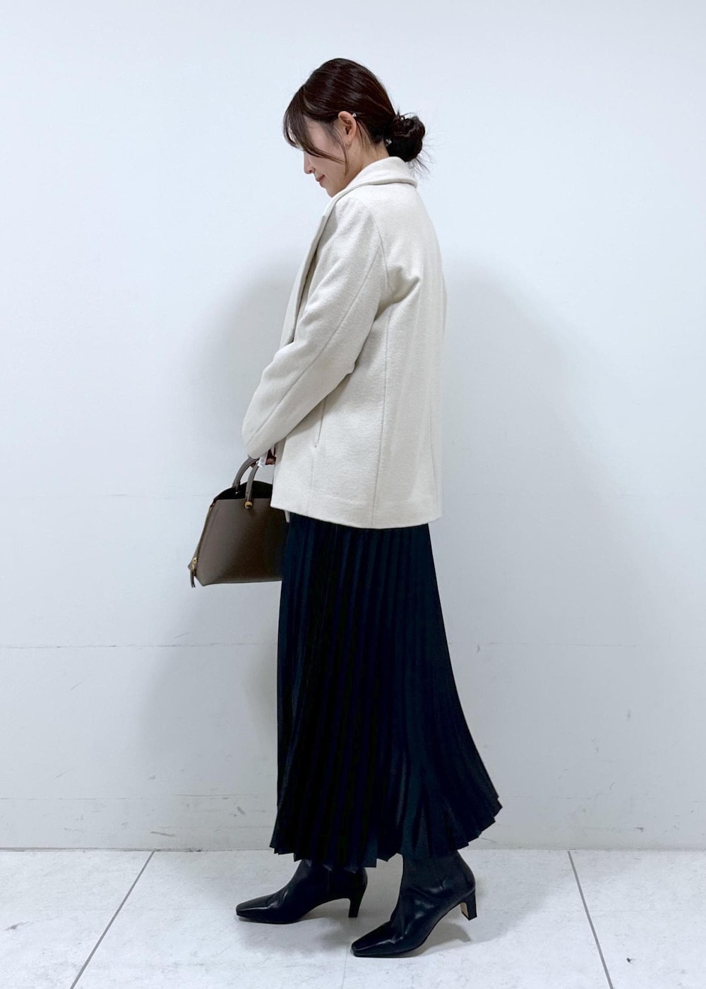 ブラック系のブーツ、ブラウン系のハンドバッグ、ホワイト系のステンカラーコートを着用したレディースの秋コーディネートの3枚目の写真