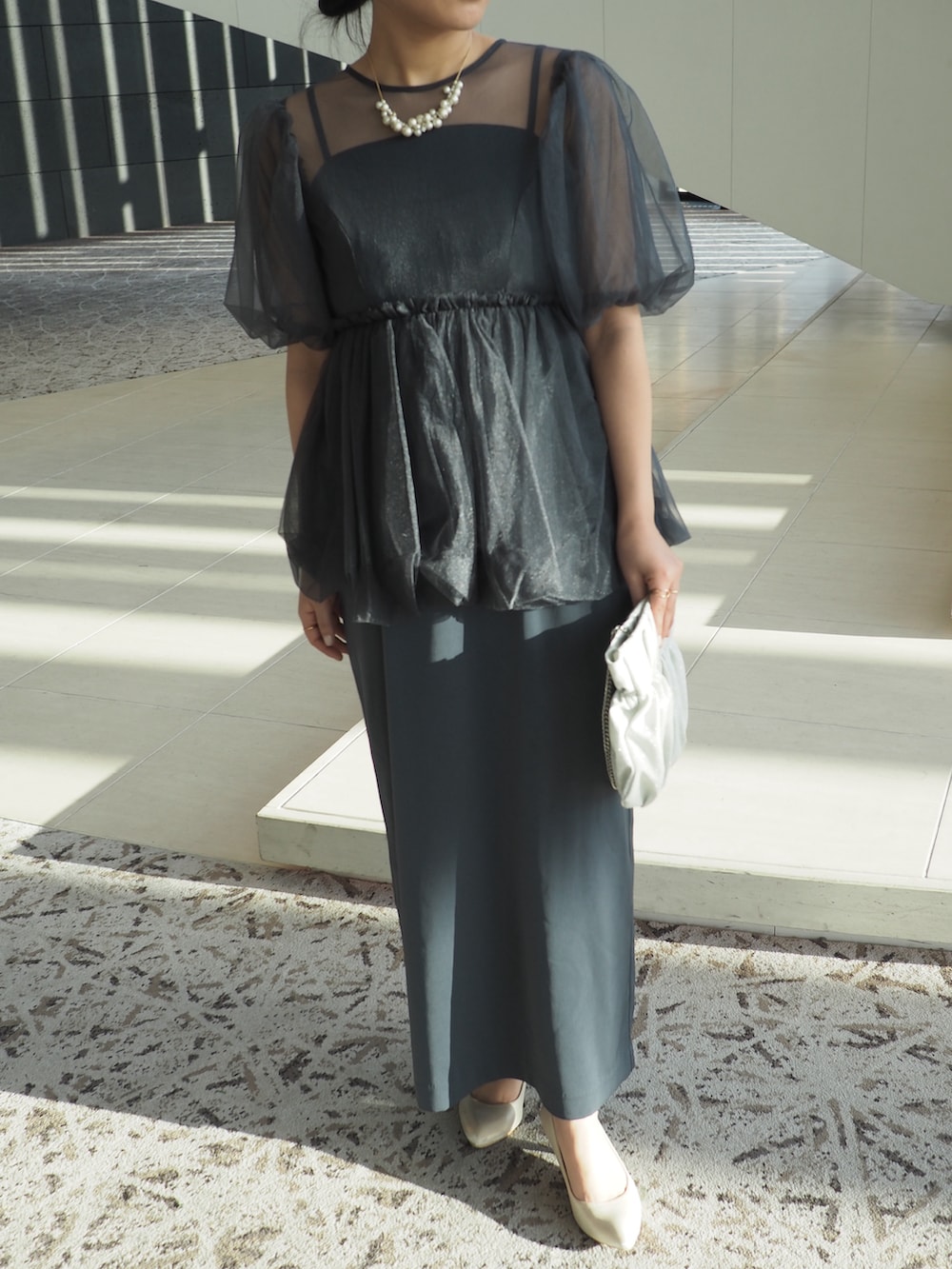 グレー系のドレス、シルバー系のクラッチバッグ、ベージュ系のパンプスを着用したレディースの冬コーディネートの3枚目の写真