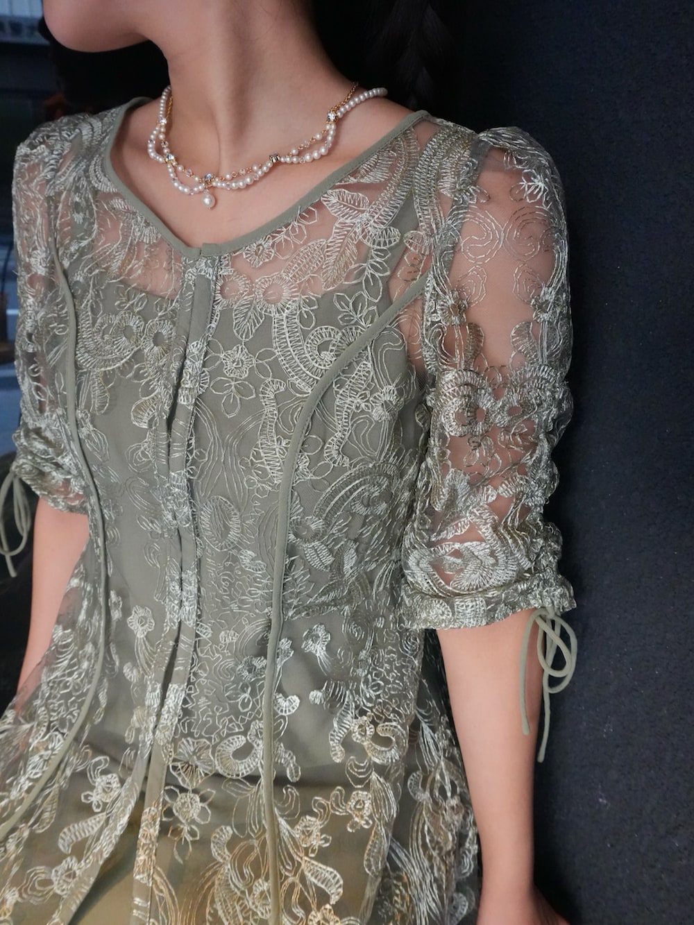 グリーン系のドレス、ブラック系のパンプス、ホワイト系のネックレスを着用したレディースの秋コーディネートの2枚目の写真