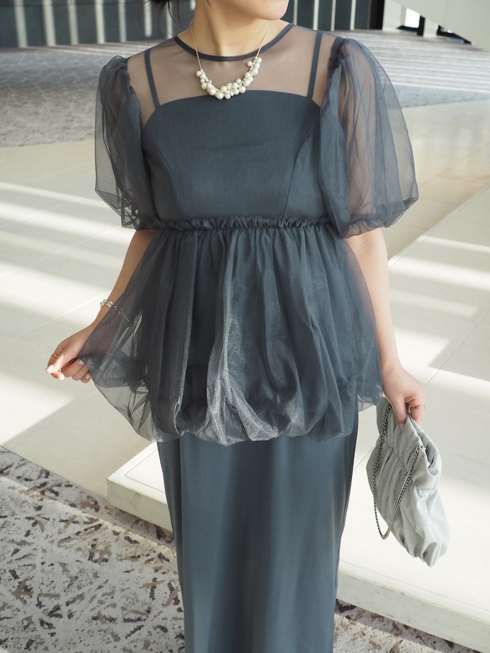 グレー系のドレス、シルバー系のクラッチバッグ、ベージュ系のパンプスを着用したレディースの冬コーディネートの2枚目の写真