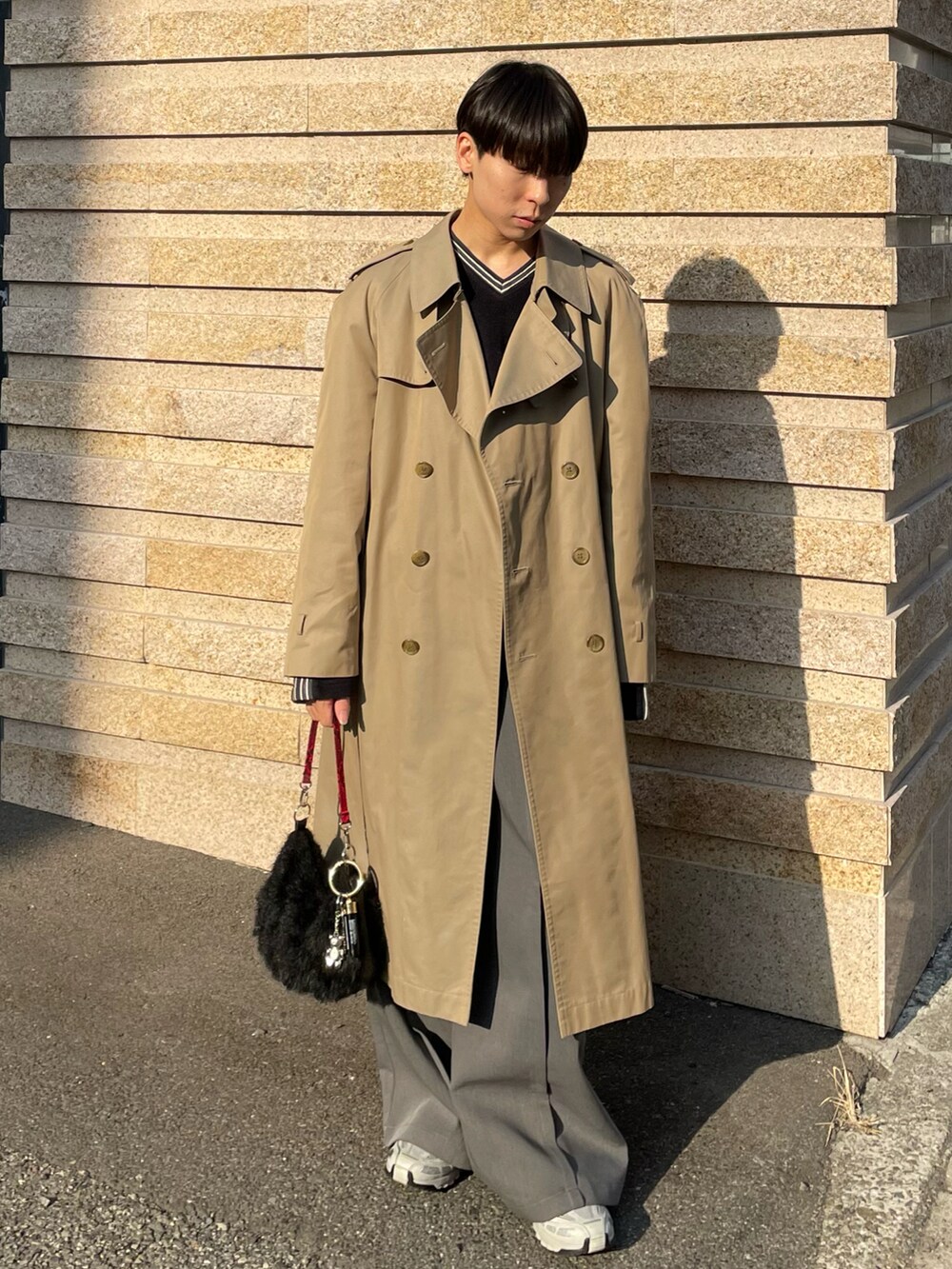 ブラック系のハンドバッグ、ベージュ系のトレンチコート、グレー系のスラックスを着用したメンズの春コーディネートの2枚目の写真